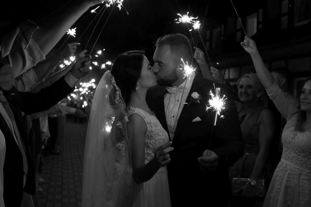 Bride and groom share a romantic kiss with sparklers, creating a magical wedding moment.